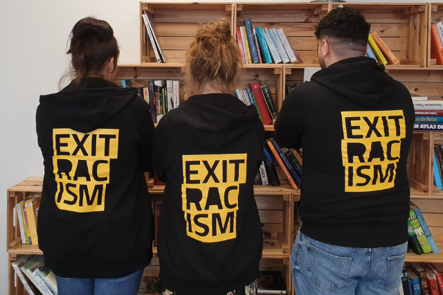 Foto von drei Personen von hinten mit einem schwarzen Pullover, der die Aufschrift "Exit Racism" trägt.