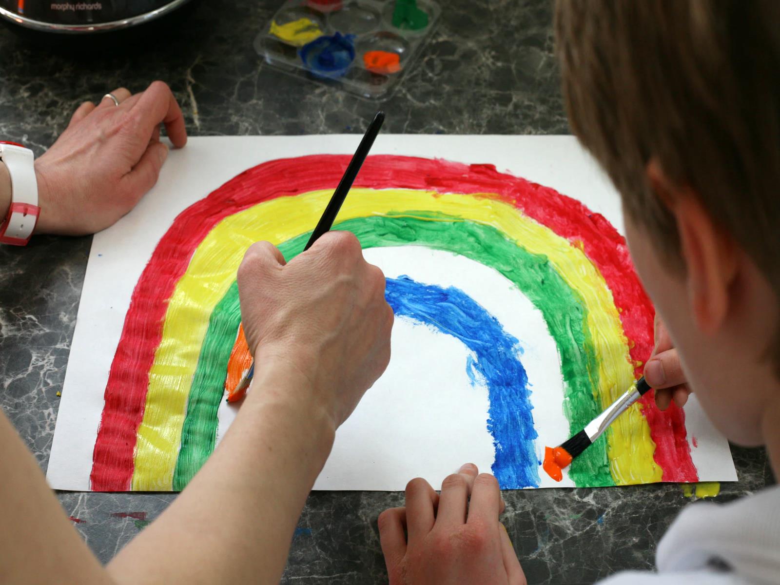 Erwachener und Kind malen regenbogen mit Wasserfarben