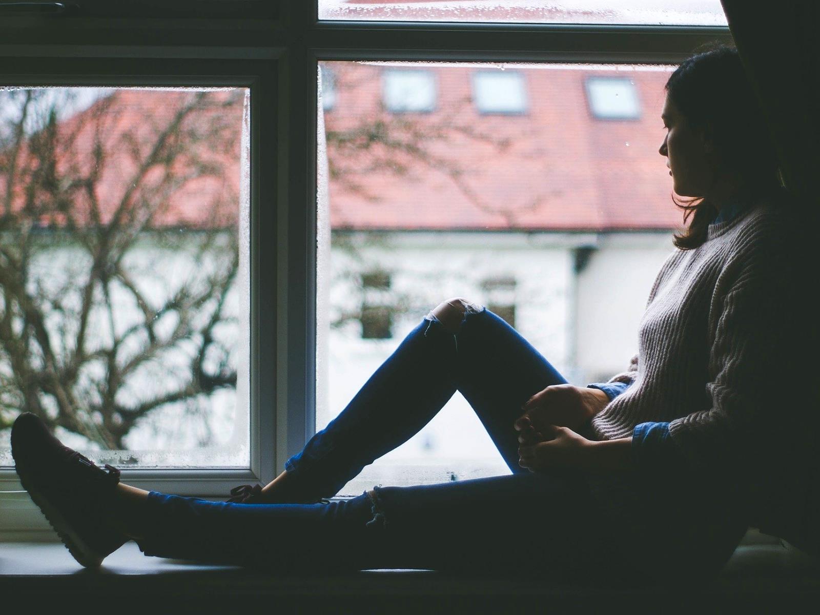Junge Frau sitzt gedankenverloren im Fenster